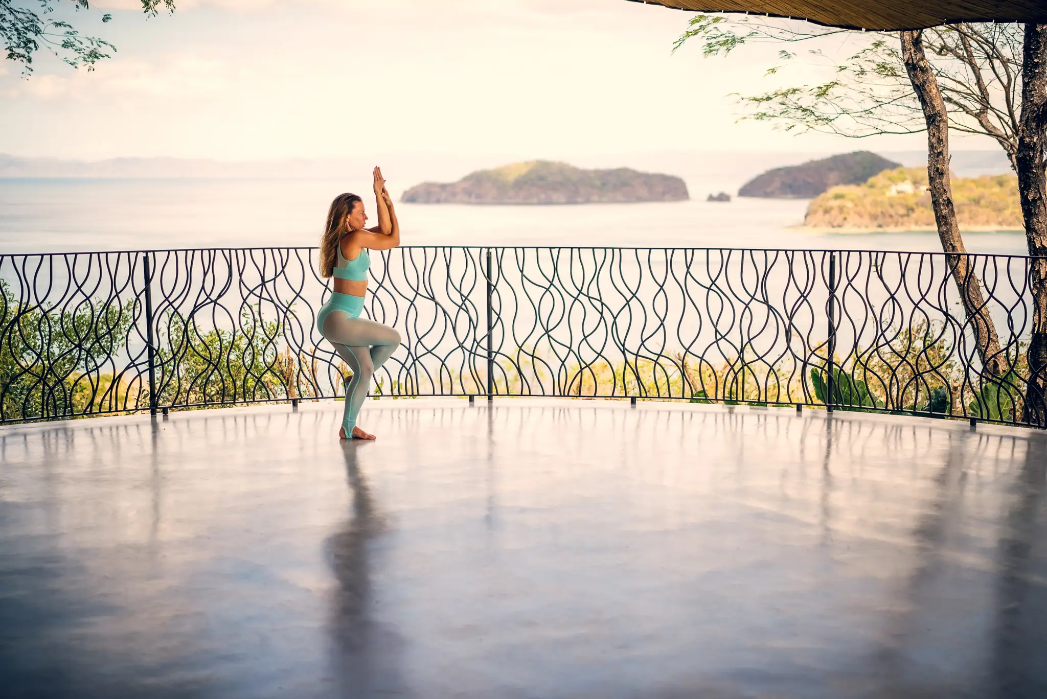 Žena v jógové pozici na terase s výhledem na moře – spojení těla, dechu a vědomí v praxi jógy